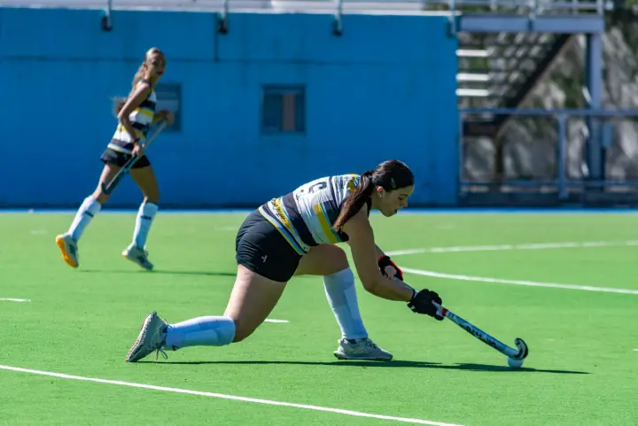 Twee volwassen hockeysters strijden om de bal op een kunstgrasveld